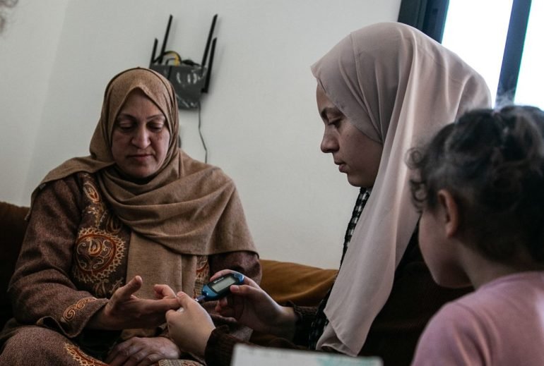 A volunteer checks a displaced woman's blood sugar levels
